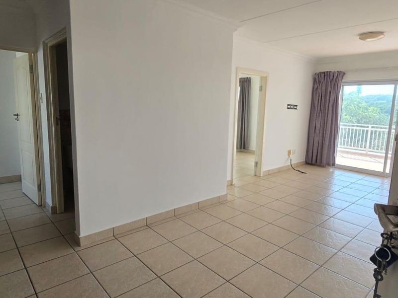 An open-plan living area featuring tiled flooring, kitchen cabinetry with granite countertops, and a sliding glass door leading to a balcony.