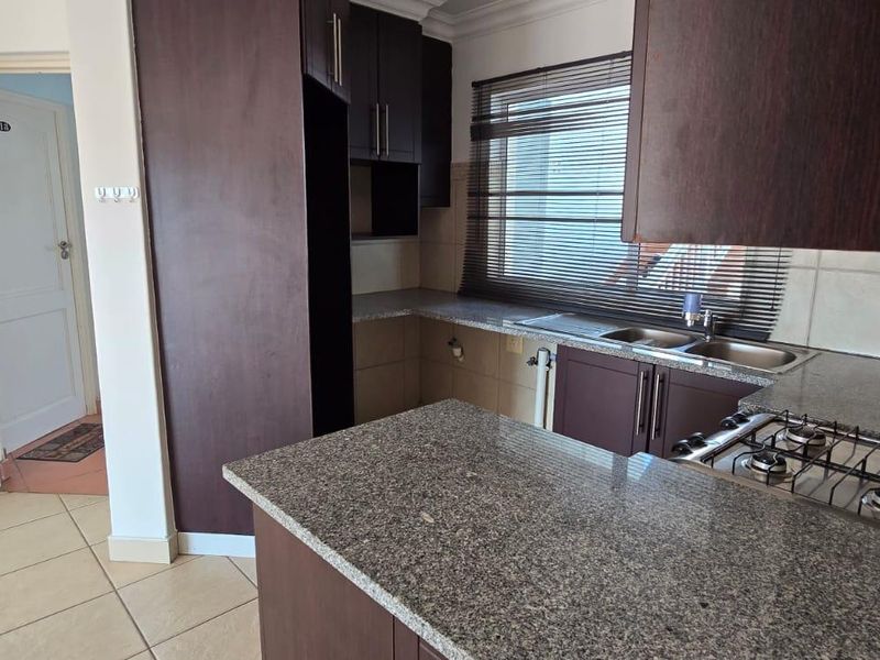 A functional kitchen featuring dark wood cabinetry, granite countertops, a gas hob, and a double basin sink with tiled flooring.