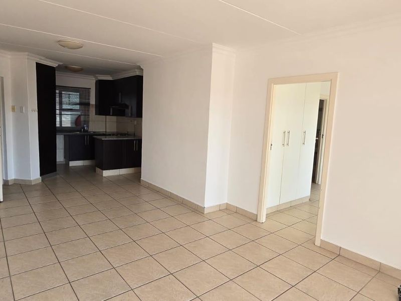 An open-plan living area featuring tiled flooring, neutral walls, and an integrated kitchen with dark cabinetry, offering a clean and versatile space.