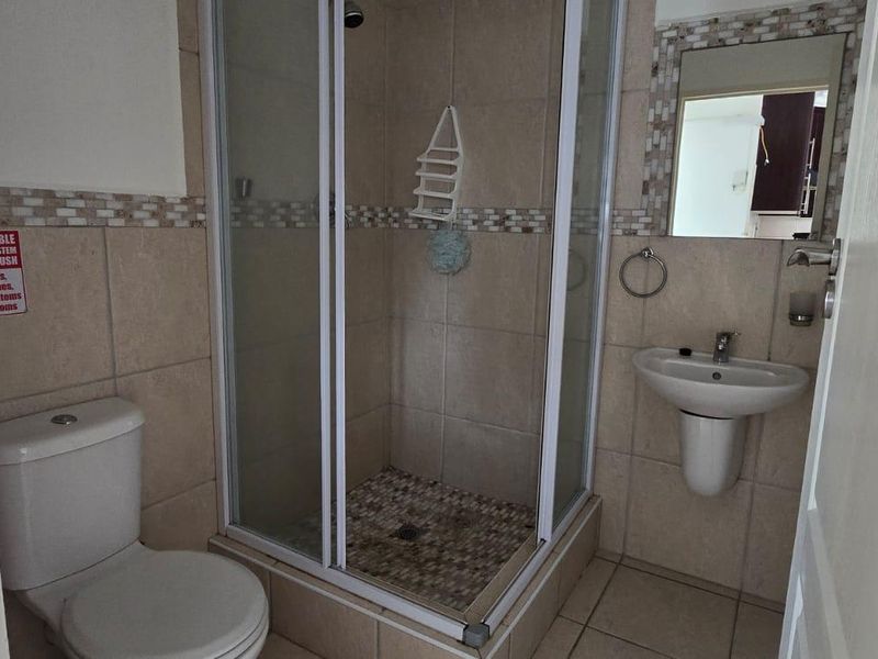 A functional bathroom featuring a shower enclosure, pedestal basin, and toilet with neutral wall and floor tiling.
