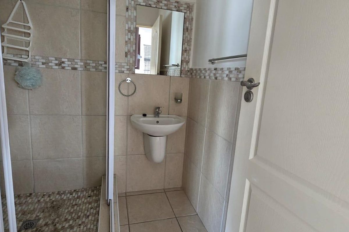 A compact bathroom featuring a wall-mounted basin, a shower enclosure with mosaic tile accents, and neutral floor-to-ceiling wall tiling.