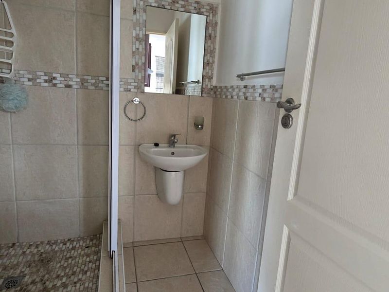 A compact bathroom featuring a wall-mounted basin, a shower enclosure with mosaic tile accents, and neutral floor-to-ceiling wall tiling.