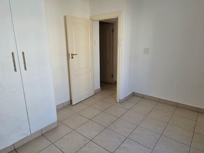 A clean, empty bedroom featuring neutral tiled flooring and a built-in white wardrobe, offering a blank canvas for personalization.