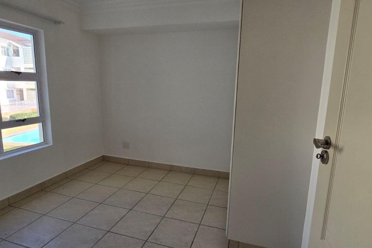 An empty bedroom featuring tiled flooring, a built-in cupboard, and a window with views of the complex pool area.