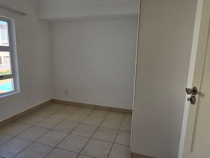 An empty bedroom featuring tiled flooring, a built-in cupboard, and a window with views of the complex pool area.