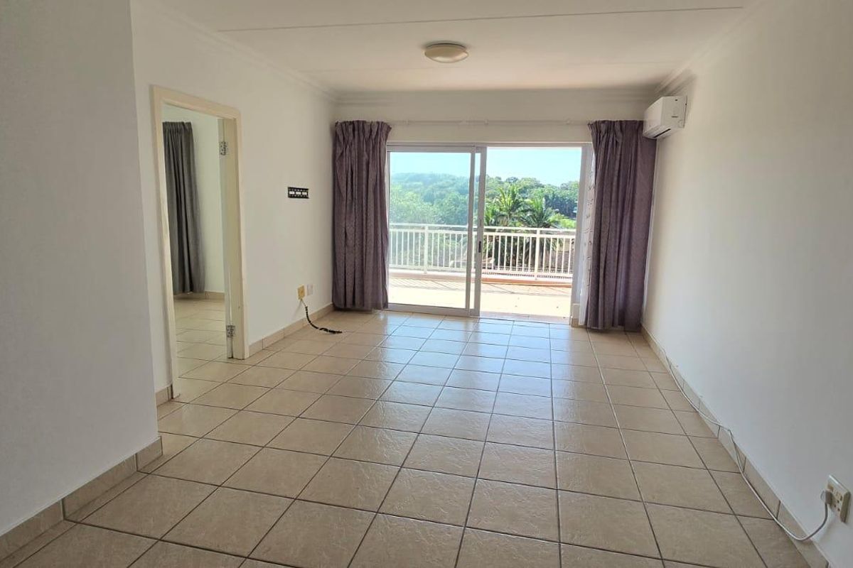 An empty living room featuring tiled flooring, an air conditioning unit, and a sliding glass door leading to a balcony with scenic views.