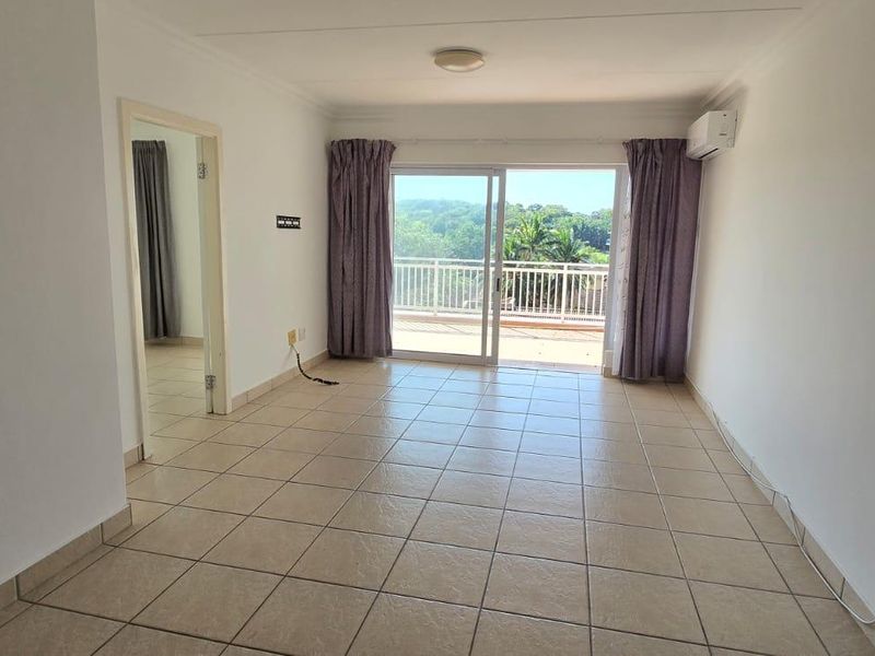 An empty living room featuring tiled flooring, an air conditioning unit, and a sliding glass door leading to a balcony with scenic views.