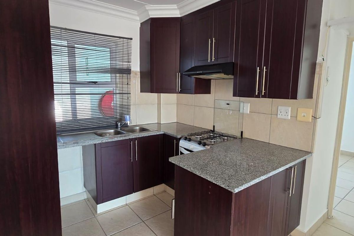 A functional kitchen featuring dark wood cabinetry, granite countertops, a gas hob with extractor fan, and tiled flooring.