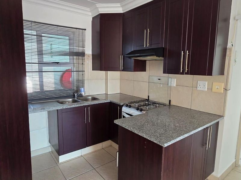 A functional kitchen featuring dark wood cabinetry, granite countertops, a gas hob with extractor fan, and tiled flooring.