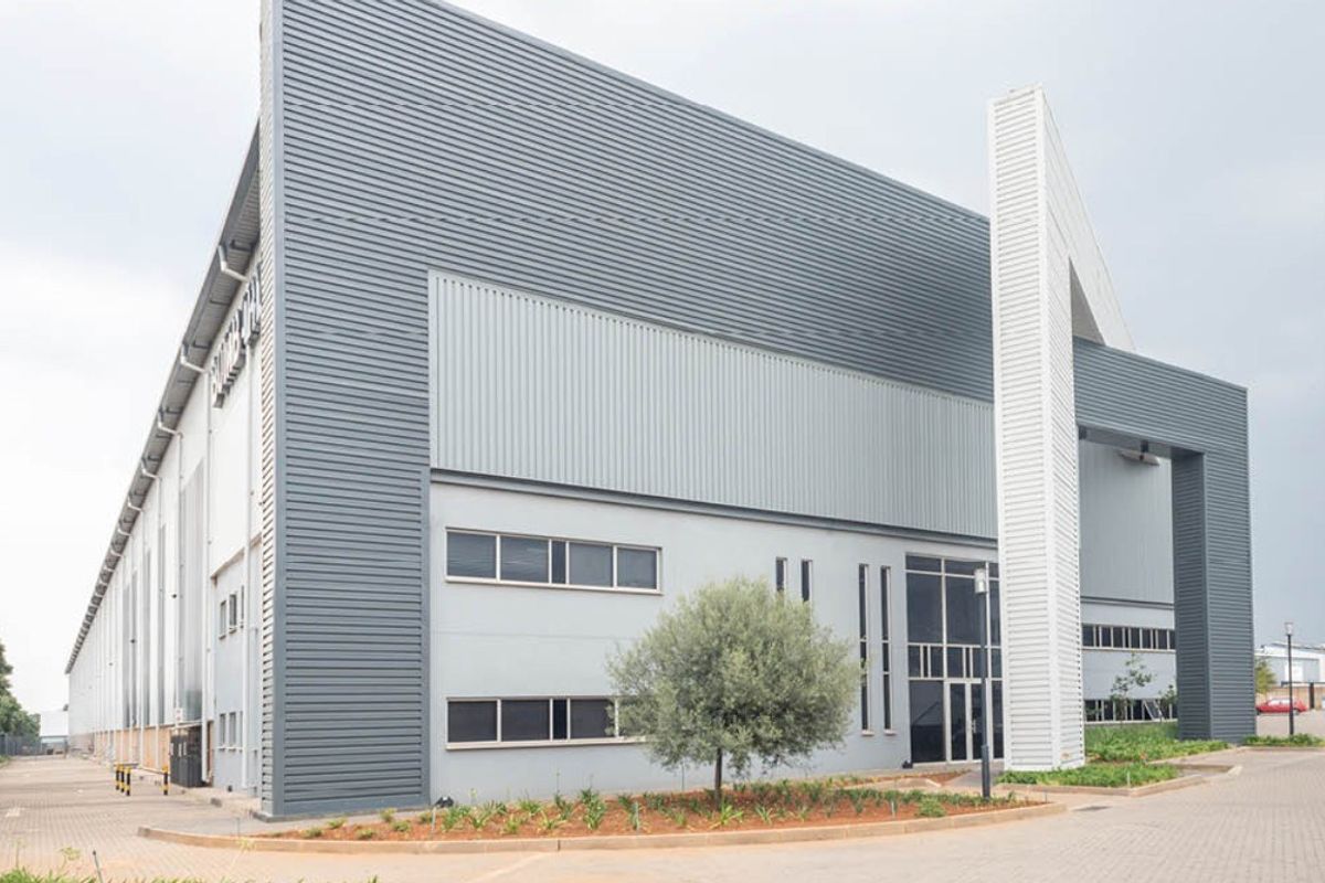 Modern industrial warehouse facility featuring corrugated metal cladding, expansive glass entrance, and paved exterior access.
