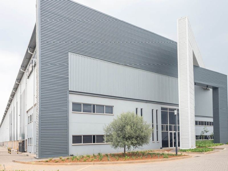Modern industrial warehouse facility featuring corrugated metal cladding, expansive glass entrance, and paved exterior access.
