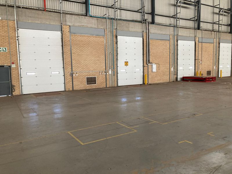 Spacious industrial warehouse interior featuring multiple roller shutter loading doors, exposed steel structural elements, and durable concrete flooring.