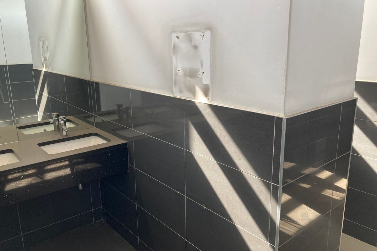A functional bathroom space featuring a double vanity with integrated sinks, chrome faucets, and dark ceramic wall tiling, currently awaiting minor cosmetic updates.