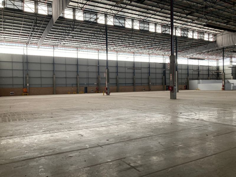 A large, open-plan industrial warehouse space featuring high ceilings, exposed steel trusses, concrete flooring, and ample natural light from clerestory windows.