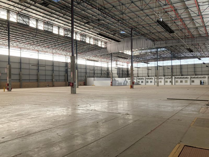 A large, open-plan industrial warehouse space featuring high ceilings, exposed steel structural elements, concrete flooring, and integrated fire safety equipment.