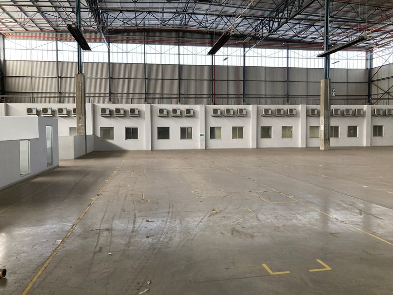 Spacious industrial warehouse interior featuring high ceilings with exposed steel trusses, concrete flooring, and multiple wall-mounted air conditioning units.