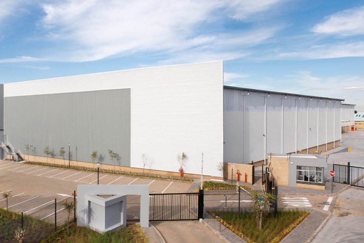 Modern industrial warehouse facility featuring extensive metal cladding, secure gated access, dedicated parking, and a guard house on a well-maintained site.