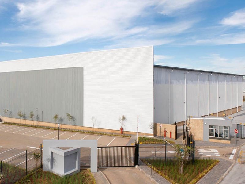 Modern industrial warehouse facility featuring extensive metal cladding, secure gated access, dedicated parking, and a guard house on a well-maintained site.