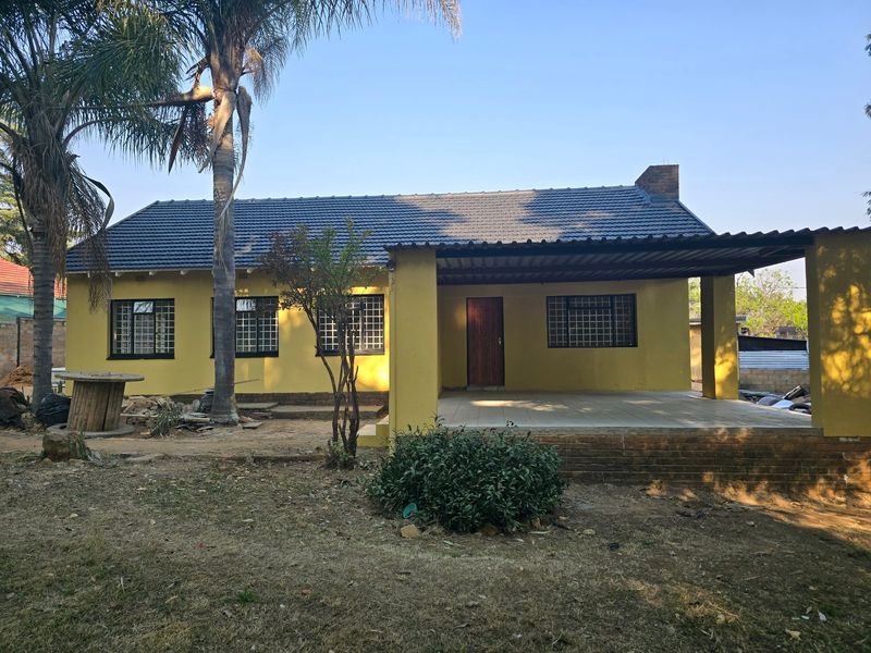 Front view of a single-story house featuring a covered patio, tiled roof, and security-barred windows, set on a large plot with established trees.