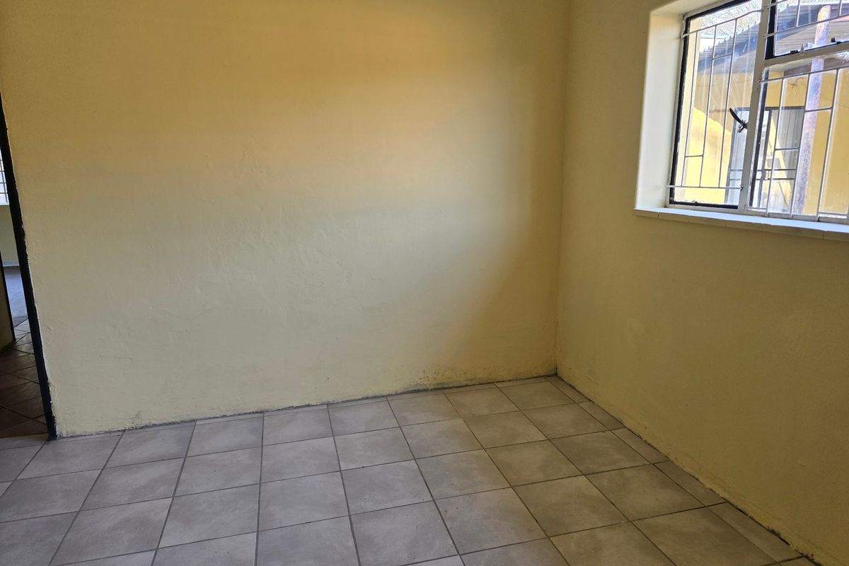 An empty bedroom featuring tiled flooring and a window with security bars, ready for a fresh coat of paint and new interior design.