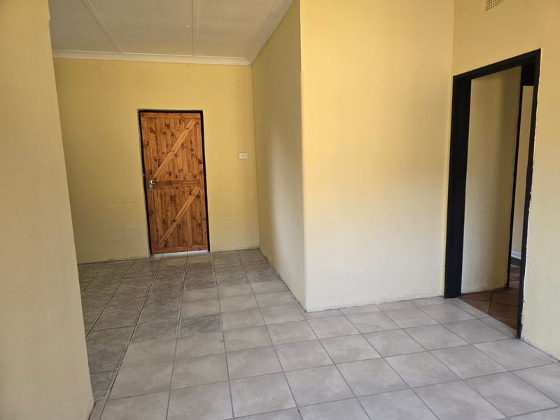 An empty living area featuring tiled flooring, a wooden door, and coved ceilings, offering a blank canvas for renovation or interior design.