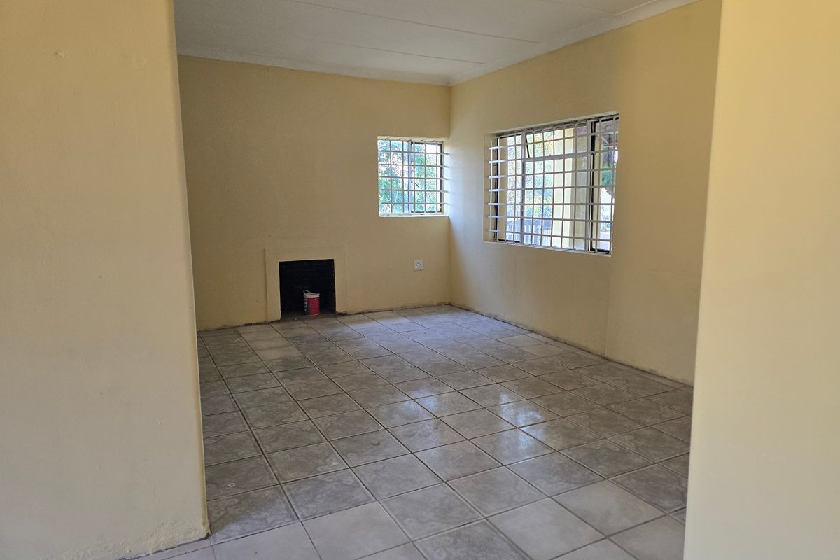 An empty living room featuring tiled flooring, a built-in fireplace, and windows fitted with security bars.