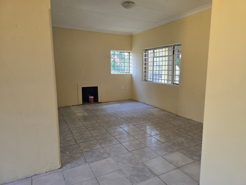 An empty living room featuring tiled flooring, a built-in fireplace, and windows fitted with security bars.
