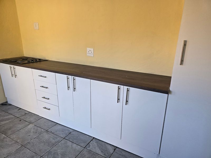 A functional kitchen area featuring white built-in cabinetry, a dark laminate countertop, an integrated electric hob, and tiled flooring.