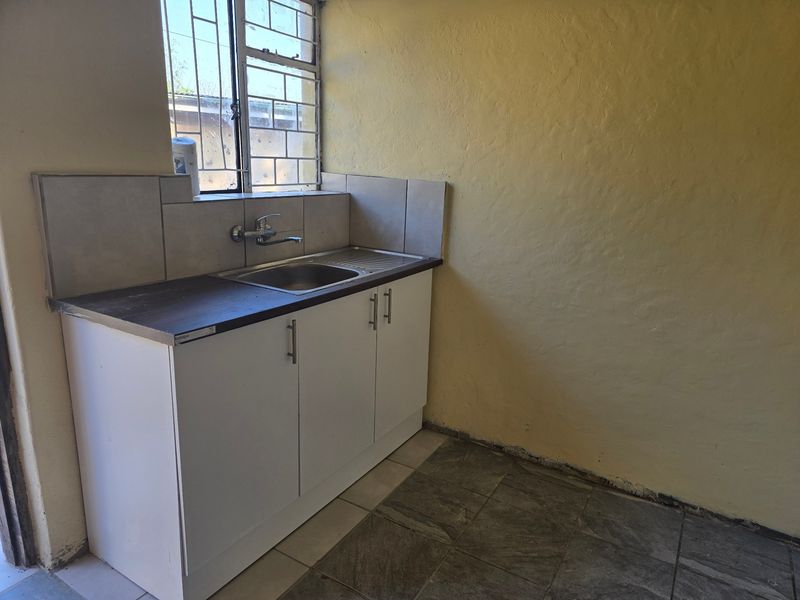 A compact kitchen area featuring a stainless steel sink, built-in base cabinetry, tiled splashback, and tiled flooring, requiring minor cosmetic updates.