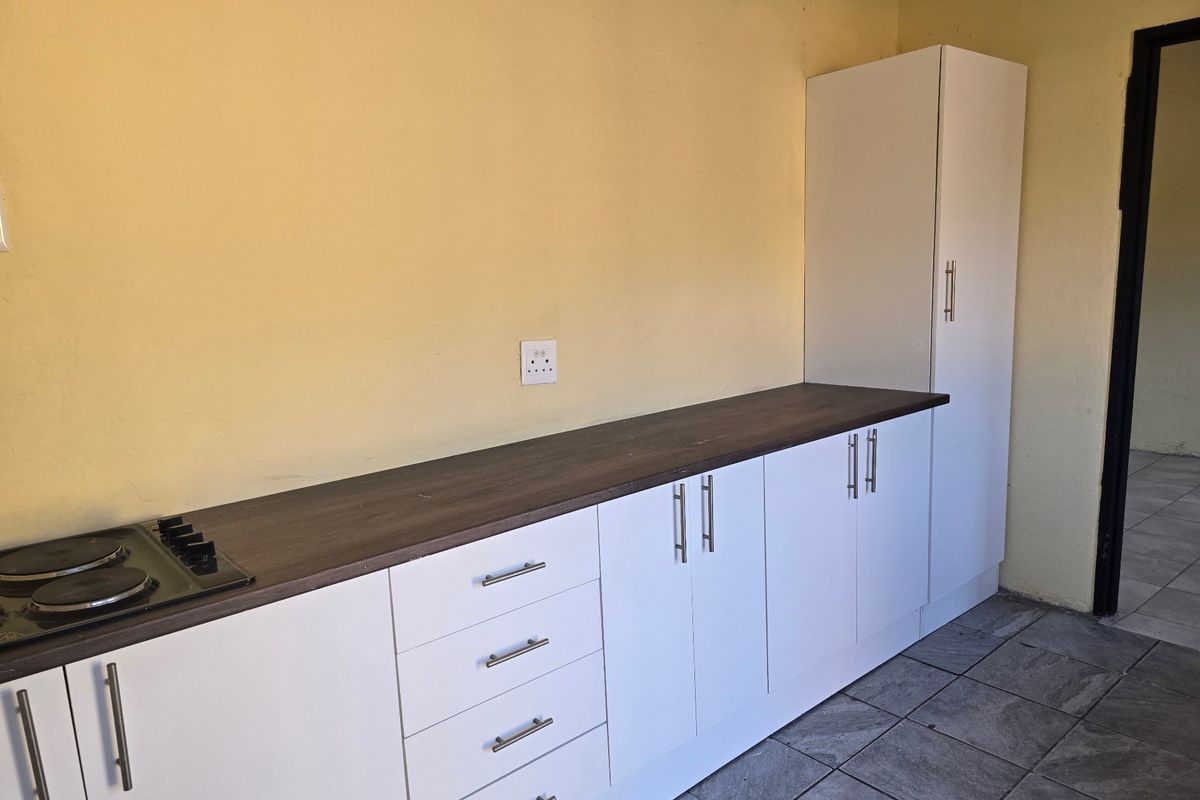 A functional kitchen area featuring white built-in cabinetry, dark laminate countertops, an integrated electric hob, and tiled flooring.