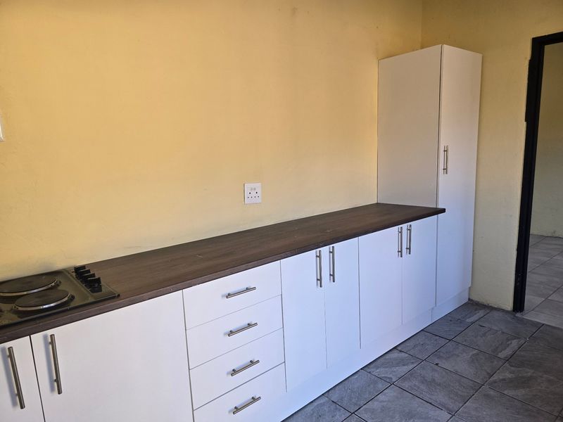A functional kitchen area featuring white built-in cabinetry, dark laminate countertops, an integrated electric hob, and tiled flooring.