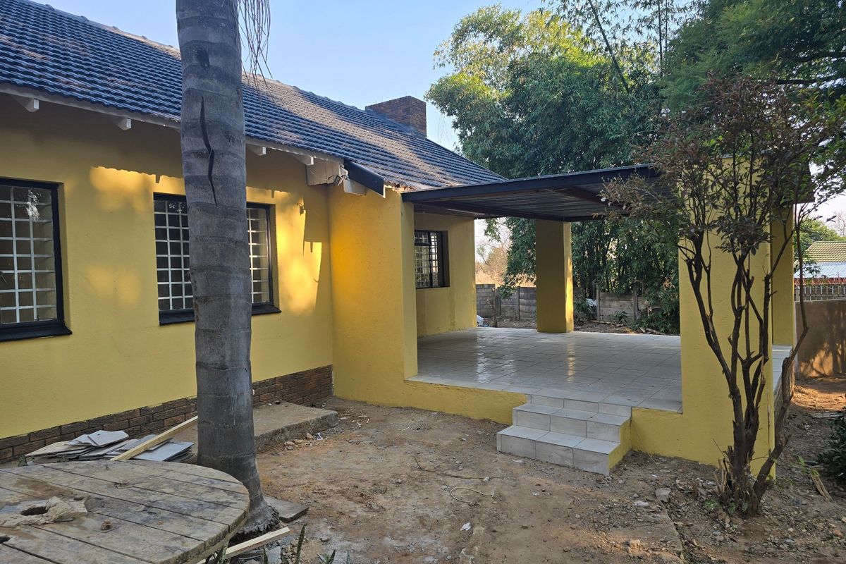 Rear view of the house featuring a covered tiled patio, brick chimney, and security-barred windows, set against a garden area.