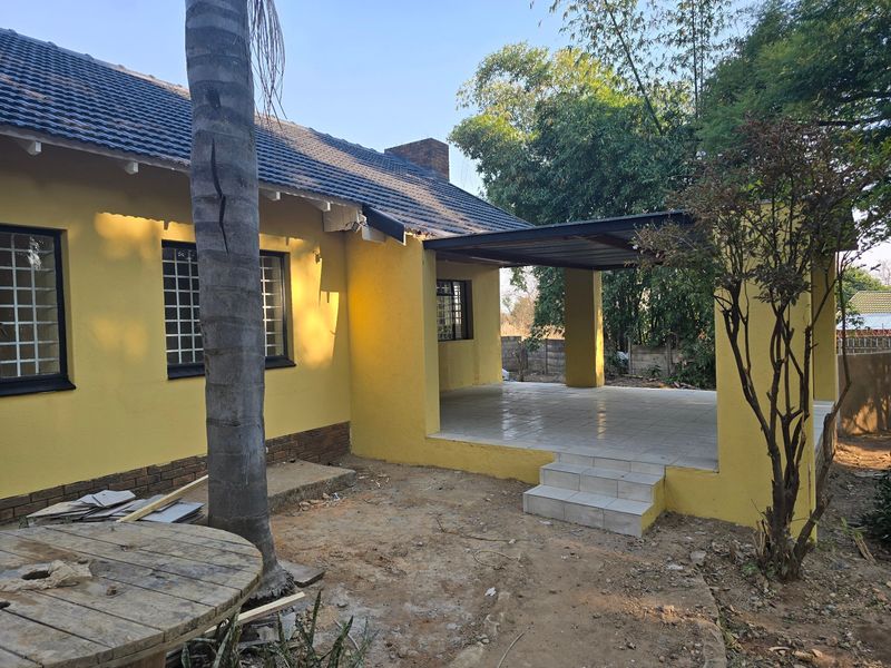 Rear view of the house featuring a covered tiled patio, brick chimney, and security-barred windows, set against a garden area.