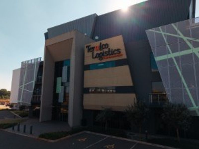 Modern industrial logistics facility featuring a contemporary facade with decorative screening, prominent commercial signage, and an asphalt parking area.