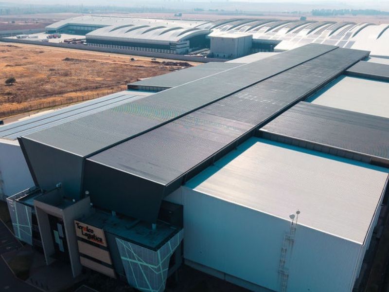 Aerial view of a large-scale industrial logistics facility featuring extensive metal roofing, integrated solar panels, and modern architectural cladding.