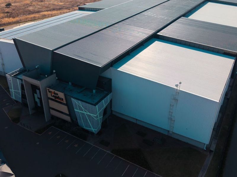 Aerial view of a modern industrial logistics facility featuring a large metal roof structure and dedicated asphalt parking area.