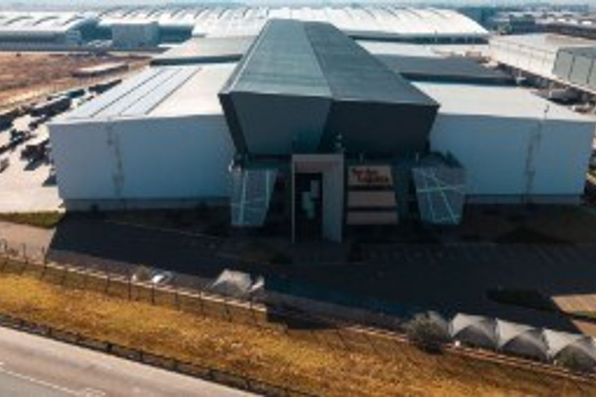 Aerial view of a large industrial warehouse facility featuring a modern facade, extensive loading areas, and secure perimeter fencing.