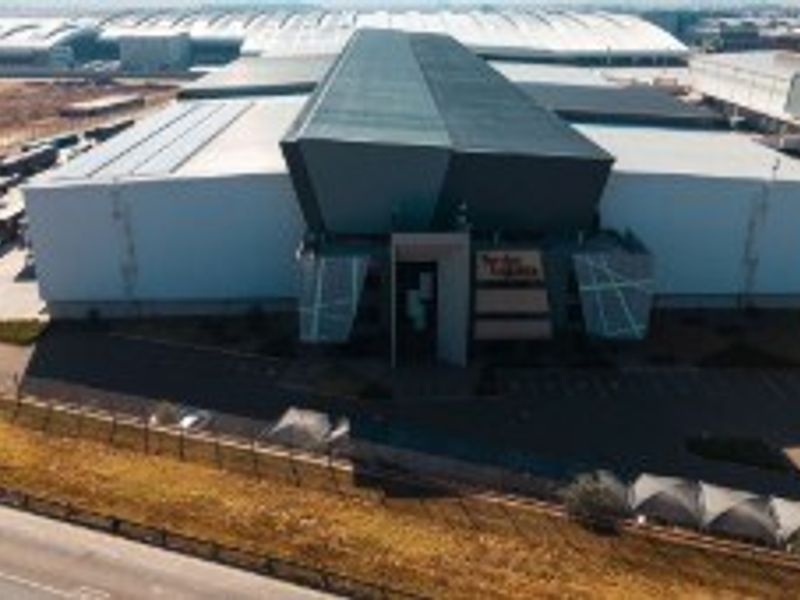 Aerial view of a large industrial warehouse facility featuring a modern facade, extensive loading areas, and secure perimeter fencing.