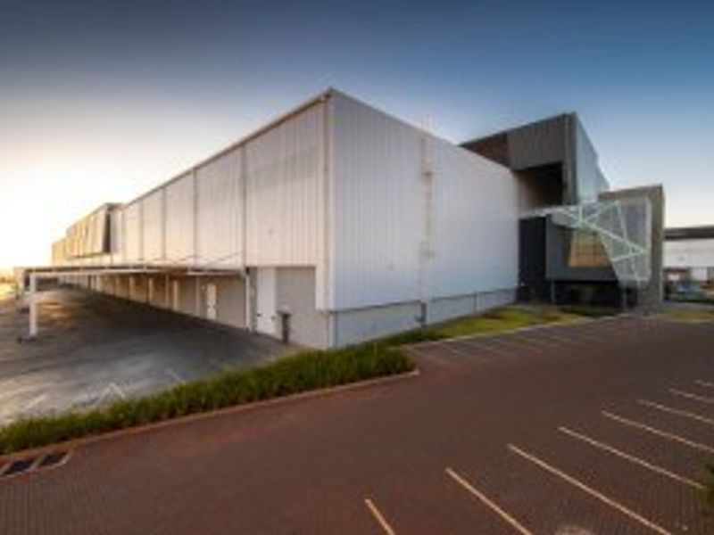 Modern industrial facility featuring extensive metal cladding, a functional loading canopy, and a spacious paved parking area for logistics and operations.