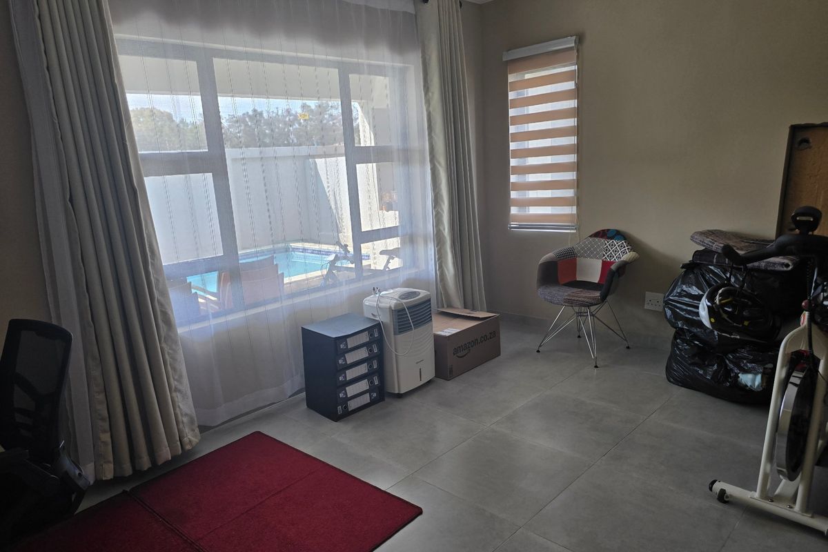 A living area featuring large windows with blinds, tiled flooring, and direct views of the outdoor pool area.