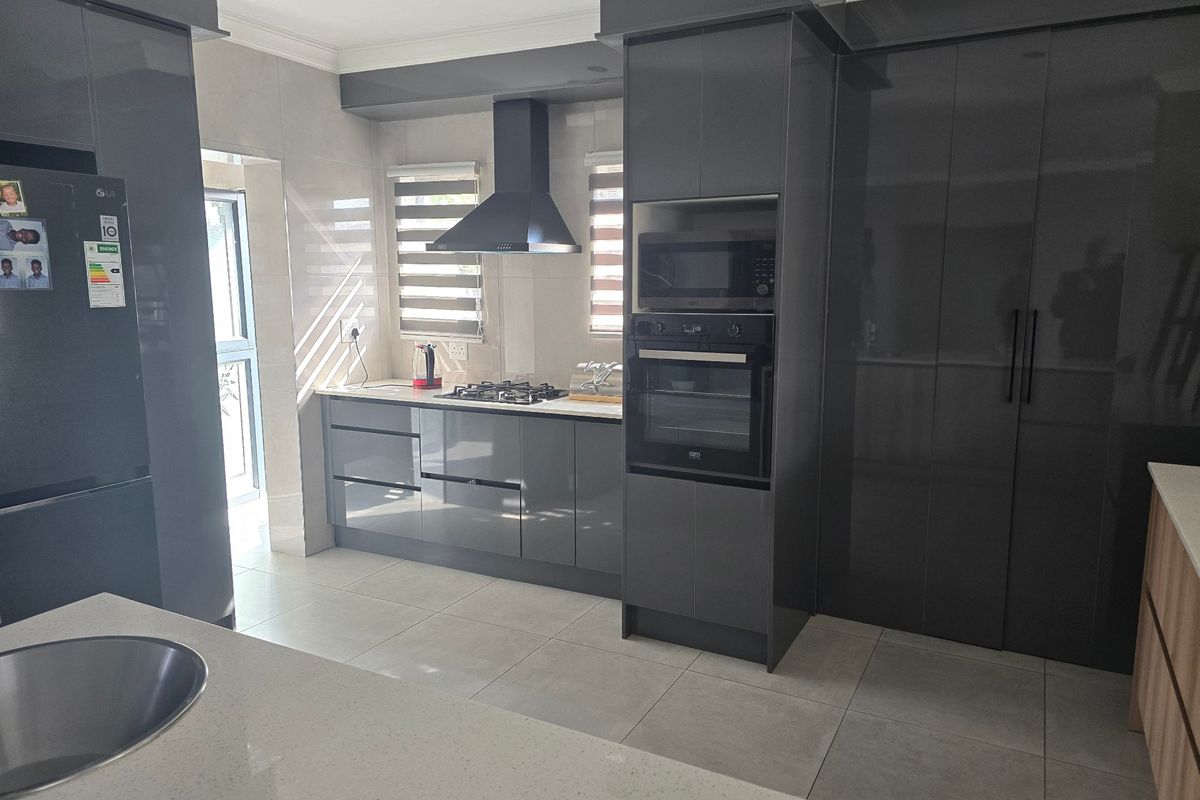 Modern kitchen featuring high-gloss grey cabinetry, stone countertops, integrated appliances including an oven and microwave, gas hob, and sleek tiled flooring.