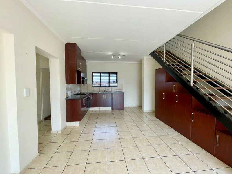 Spacious open-plan kitchen and living area featuring dark wood cabinetry, granite countertops, tiled flooring, and a modern staircase with integrated under-stair storage.