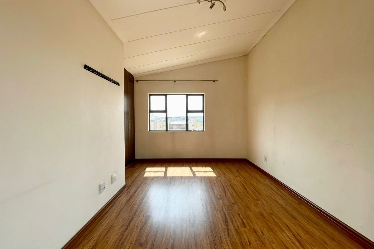 An empty bedroom featuring laminate flooring, built-in cupboards, and a window with natural light, offering a clean and neutral space ready for personalization.