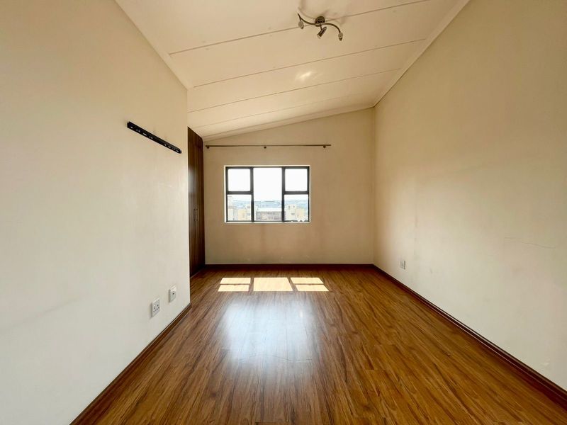 An empty bedroom featuring laminate flooring, built-in cupboards, and a window with natural light, offering a clean and neutral space ready for personalization.