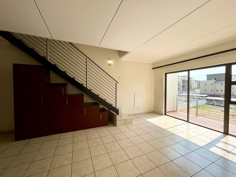 Spacious open-plan living area featuring tiled floors, a staircase with built-in storage, and large sliding doors leading to a private balcony.