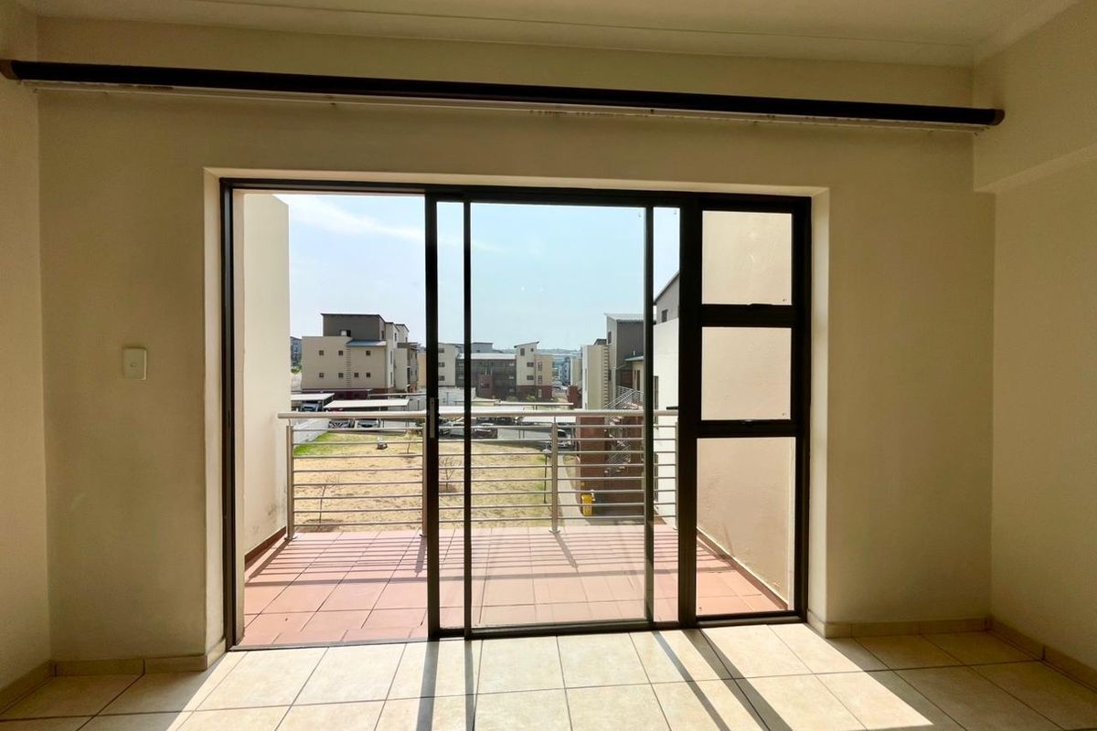 Bright and empty living area featuring large sliding glass doors that open onto a private balcony with neighborhood views.