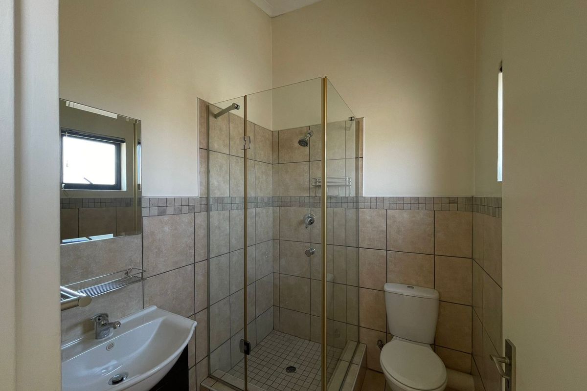 A functional bathroom featuring a glass-enclosed shower, wall-mounted basin, and toilet with neutral wall and floor tiling.