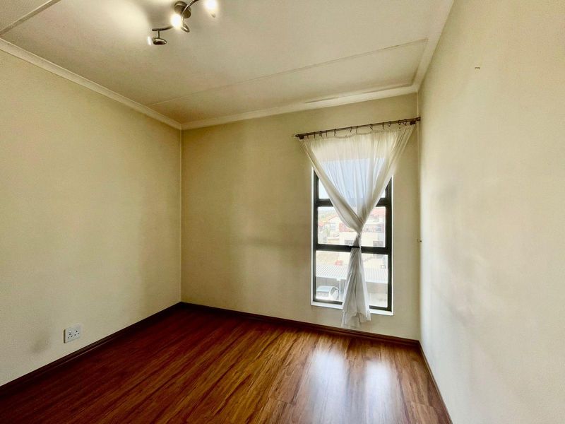A bright, empty bedroom featuring laminate wood flooring, neutral walls, and a vertical window providing natural light.