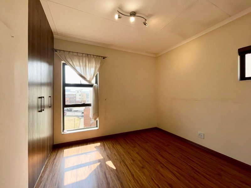 An empty bedroom featuring laminate flooring, built-in cupboards, and a window with natural light.