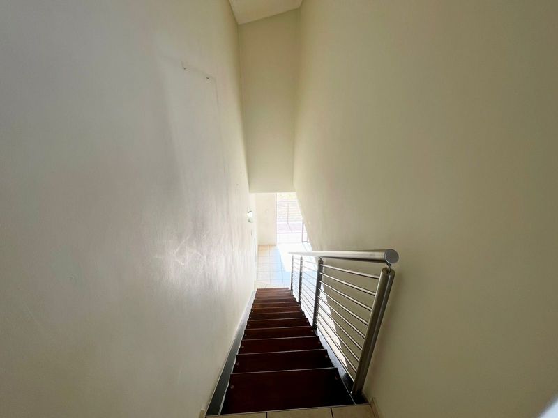 A functional staircase featuring a modern stainless steel balustrade, leading down to a tiled landing area.